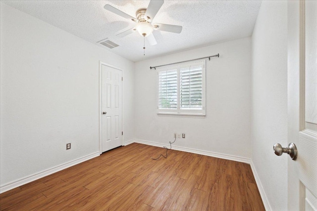 empty room with wood finished floors, a textured ceiling, baseboards, and visible vents