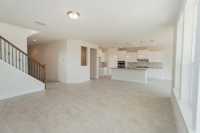 313 Singing Dove Way, Liberty Hill, TX 78642 - unfurnished living room with visible vents, a sink, and stairway