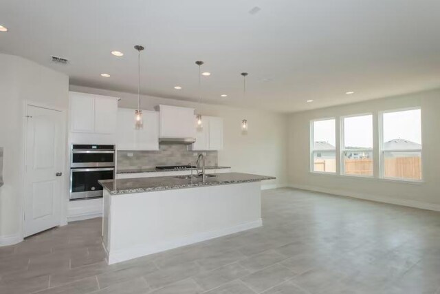 313 Singing Dove Way, Liberty Hill, TX 78642 - kitchen with white cabinets, double oven, visible vents, stone countertops, and decorative backsplash