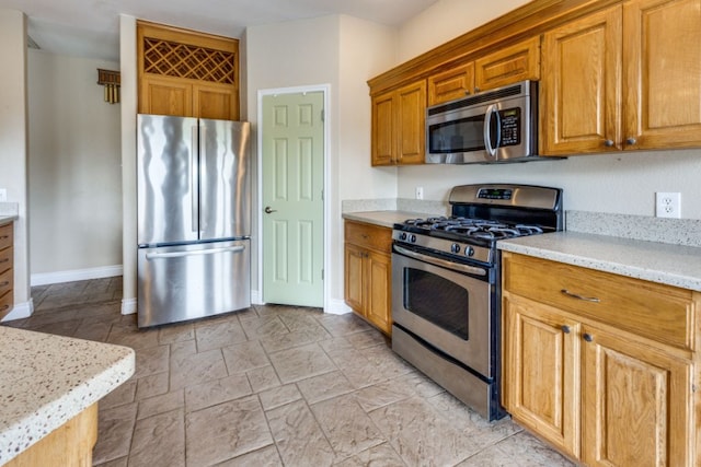 208 Saddletree Ln, Dripping Springs, TX 78620 - kitchen with stainless steel appliances, baseboards, light stone counters, and brown cabinets