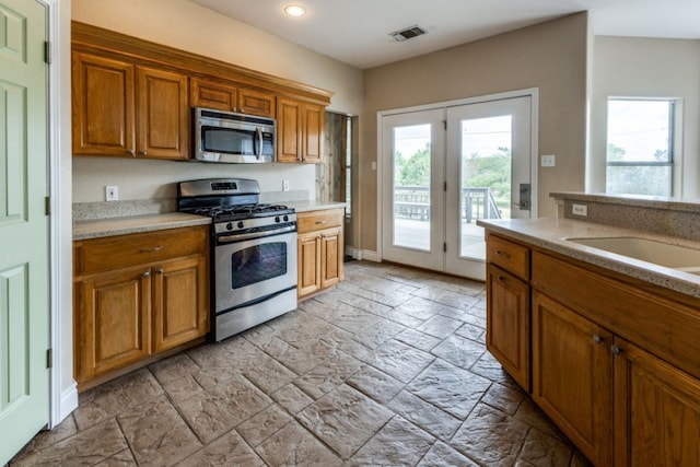 208 Saddletree Ln, Dripping Springs, TX 78620 - kitchen featuring appliances with stainless steel finishes, stone tile flooring, brown cabinetry, light countertops, and recessed lighting