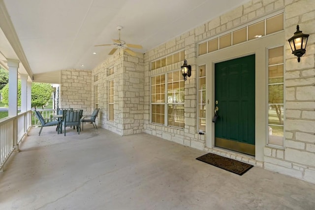 view of exterior entry with a ceiling fan, stone siding, and covered porch