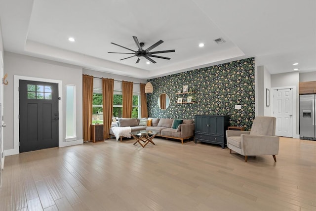 living room with wallpapered walls, an accent wall, ceiling fan, visible vents, and a raised ceiling
