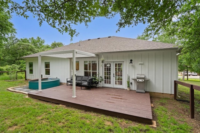 rear view of property featuring hot tub deck surround, a deck, a lawn, and french doors