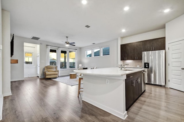 kitchen with a sink, open floor plan, dark brown cabinetry, a center island with sink, and appliances with stainless steel finishes