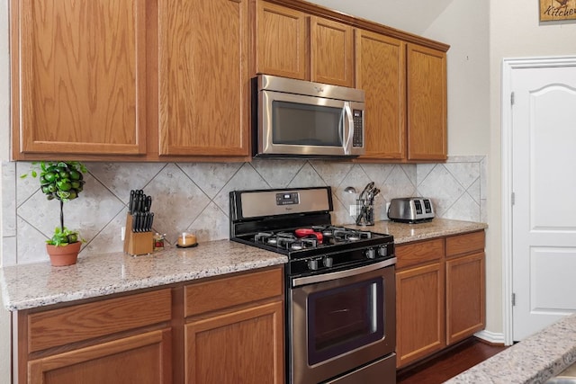535 Tranquility Mtn, Buda, TX 78610 - kitchen with appliances with stainless steel finishes, tasteful backsplash, light stone counters, and brown cabinets