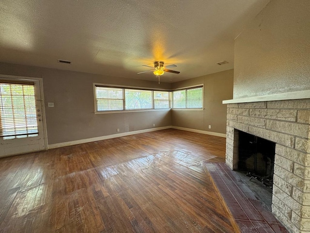 unfurnished living room featuring a stone fireplace, visible vents, a ceiling fan, dark wood-type flooring, and baseboards