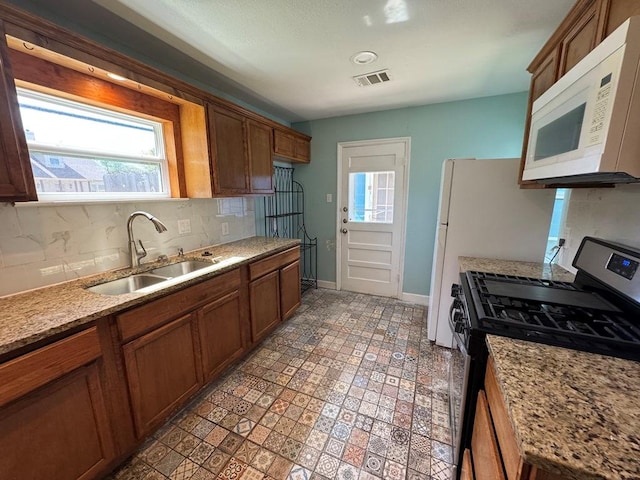 kitchen with a sink, visible vents, white microwave, decorative backsplash, and stainless steel gas range oven