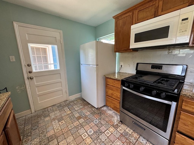 kitchen with tasteful backsplash, brown cabinetry, white appliances, stone counters, and baseboards
