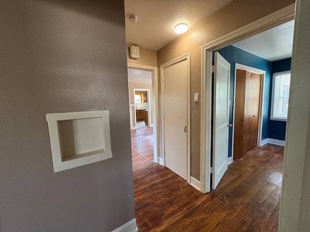 hall featuring baseboards, a textured wall, wood finished floors, and plenty of natural light