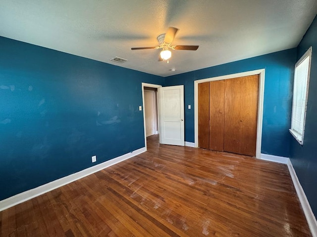 unfurnished bedroom featuring wood finished floors, visible vents, a ceiling fan, a closet, and baseboards