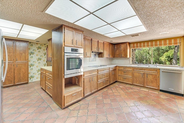 9401 Cedar Crest Dr, Austin, TX 78750 - kitchen with appliances with stainless steel finishes, light countertops, wallpapered walls, brown cabinets, and a sink