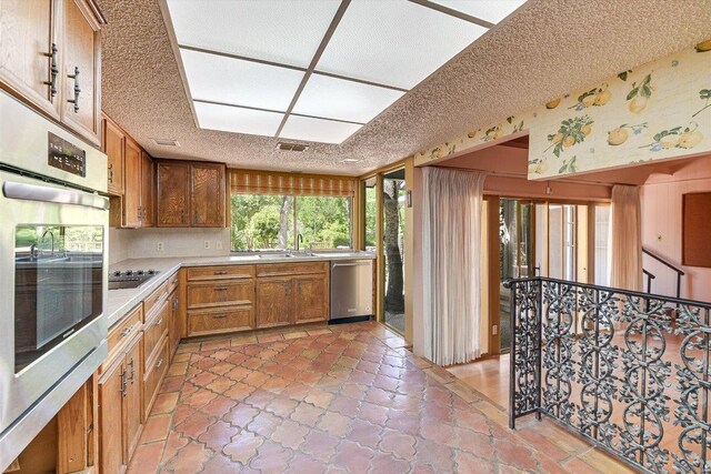 9401 Cedar Crest Dr, Austin, TX 78750 - kitchen with appliances with stainless steel finishes, light countertops, a sink, a textured ceiling, and brown cabinetry