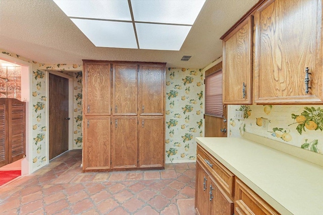 9401 Cedar Crest Dr, Austin, TX 78750 - kitchen with wallpapered walls, baseboards, light countertops, brown cabinets, and light tile patterned flooring