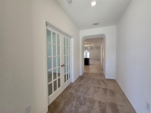 corridor with arched walkways, carpet floors, french doors, baseboards, and visible vents