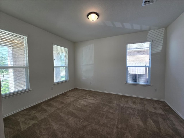 spare room with dark carpet, visible vents, and a healthy amount of sunlight