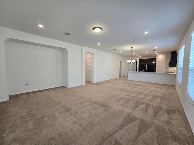unfurnished living room featuring recessed lighting, visible vents, arched walkways, light colored carpet, and a notable chandelier