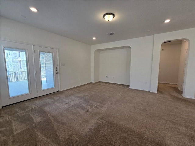 carpeted empty room with baseboards, visible vents, arched walkways, and recessed lighting