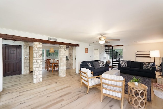 living area featuring ornate columns, visible vents, light wood-style floors, stairs, and ceiling fan