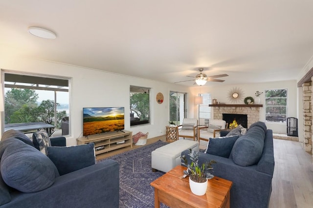 living room with wood finished floors, a wealth of natural light, a ceiling fan, and a lit fireplace