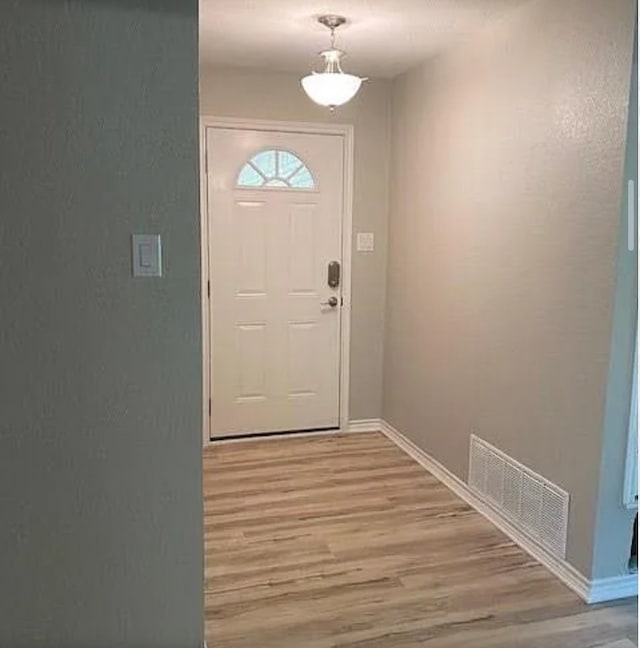 doorway with baseboards, light wood finished floors, and visible vents