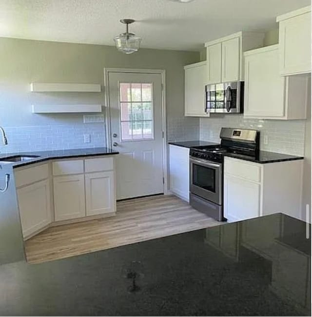 kitchen featuring stainless steel appliances, a sink, light wood-style flooring, tasteful backsplash, and white cabinetry