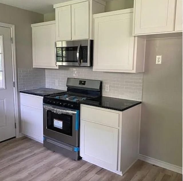 kitchen featuring dark countertops, stainless steel appliances, white cabinetry, and light wood-type flooring
