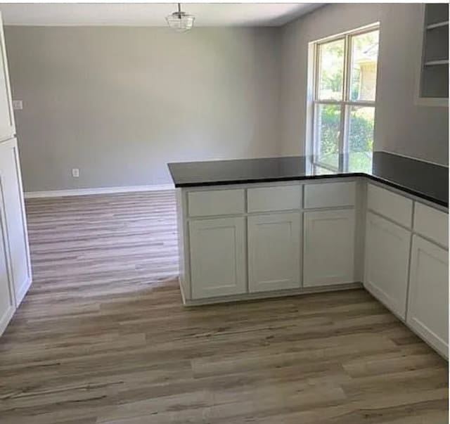 kitchen with white cabinets, a peninsula, dark countertops, and light wood-style floors