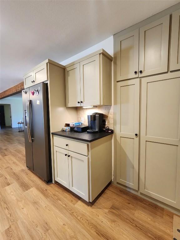 kitchen with backsplash, stainless steel fridge, dark countertops, and light wood-style floors