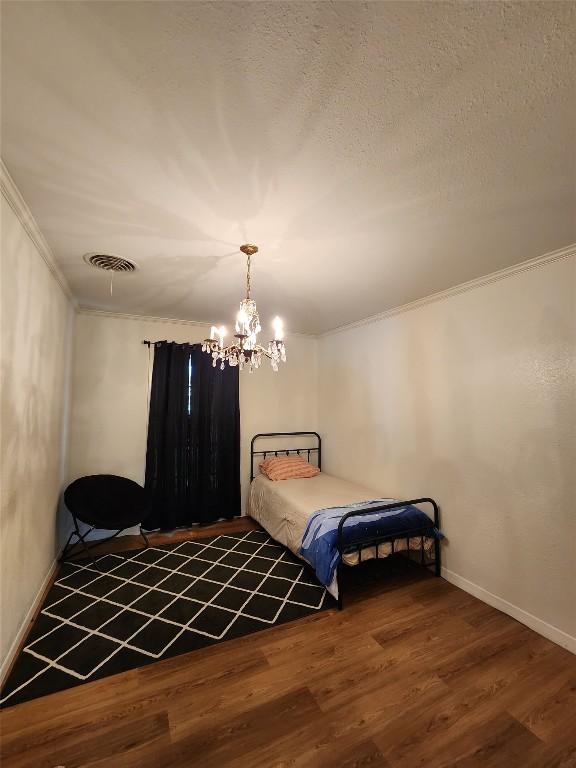 bedroom featuring wood finished floors, visible vents, crown molding, baseboards, and a chandelier