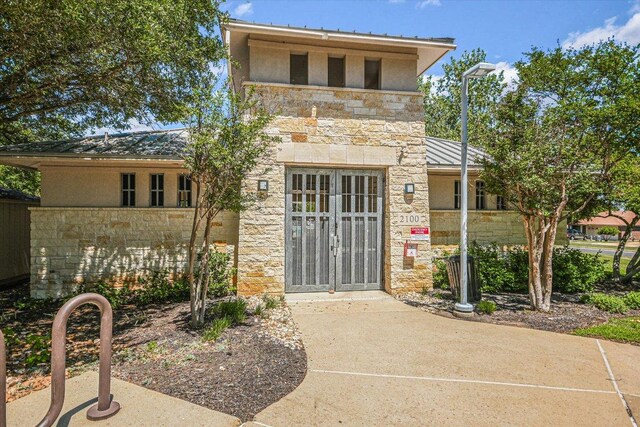 view of exterior entry featuring stone siding, a standing seam roof, and stucco siding