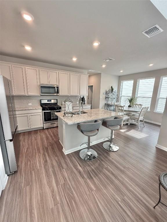 793 Lone Peak Way, Dripping Springs, TX 78620 - kitchen with stainless steel appliances, dark wood-type flooring, a kitchen breakfast bar, decorative backsplash, and white cabinets