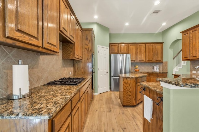 3820 Lagoona Dr, Round Rock, TX 78681 - kitchen with freestanding refrigerator, gas cooktop, light wood finished floors, brown cabinetry, and dark stone counters