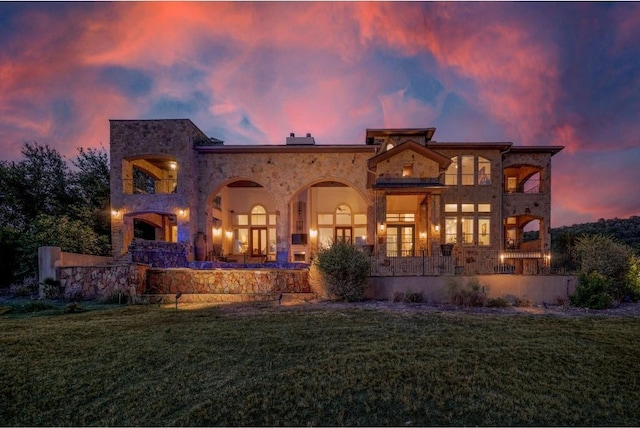 8315 Lime Creek Rd, Volente, TX 78641 - back of house at dusk featuring a lawn, stone siding, and a balcony