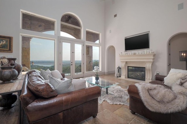 8315 Lime Creek Rd, Volente, TX 78641 - living room with arched walkways, a towering ceiling, stone tile flooring, french doors, and a glass covered fireplace