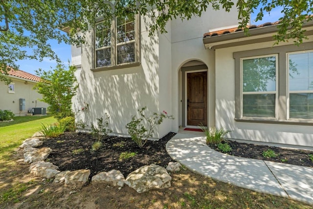 doorway to property with a tiled roof, central air condition unit, and stucco siding