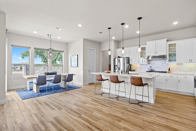 kitchen featuring stovetop, baseboards, under cabinet range hood, and stainless steel fridge