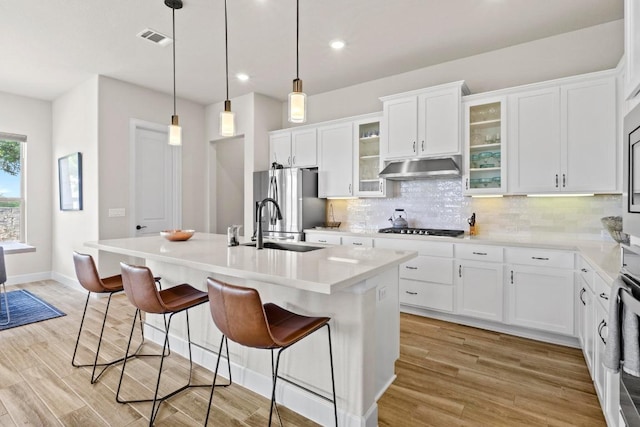 kitchen with a sink, tasteful backsplash, freestanding refrigerator, visible vents, and under cabinet range hood