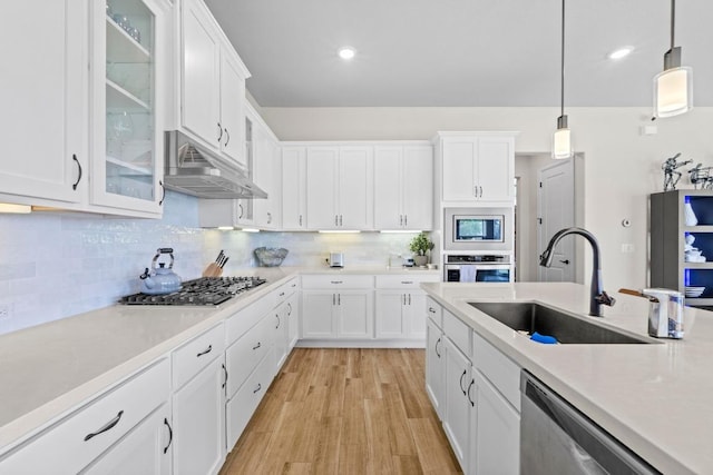 kitchen with stainless steel appliances, light countertops, under cabinet range hood, and a sink