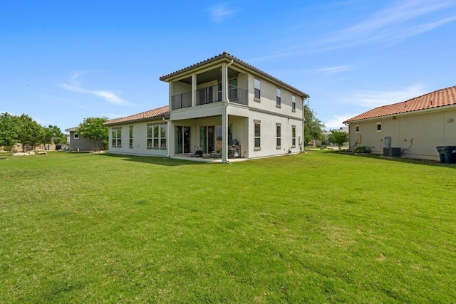 back of property with a balcony, a lawn, central air condition unit, a patio, and stucco siding