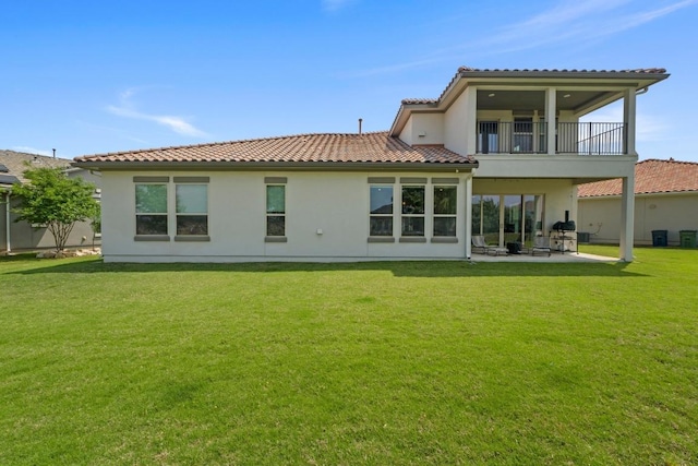 rear view of property featuring a tiled roof, a balcony, stucco siding, a patio, and a lawn