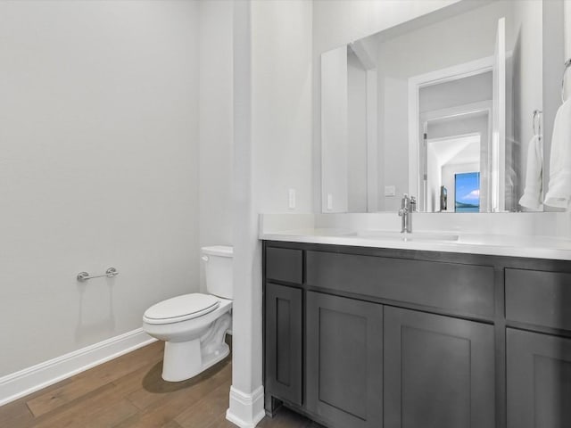 half bathroom featuring toilet, vanity, wood finished floors, and baseboards
