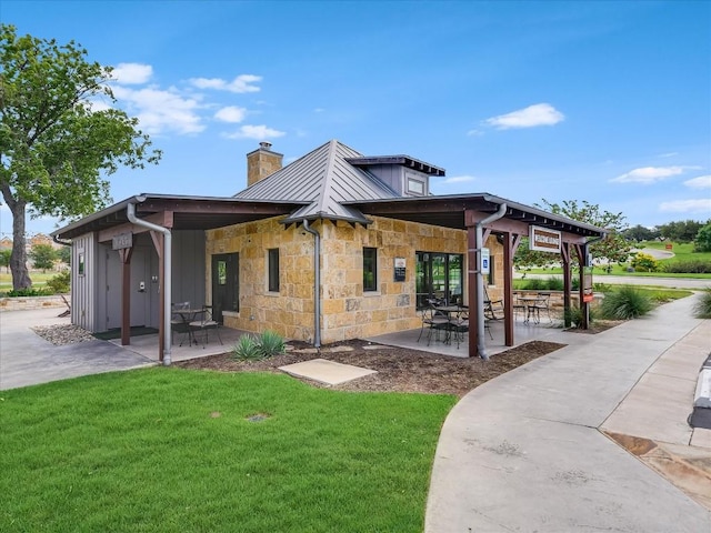 back of property featuring a yard, stone siding, a chimney, and a patio