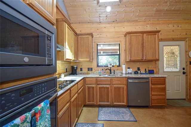 kitchen featuring stainless steel appliances, a sink, vaulted ceiling, wood walls, and light stone counters