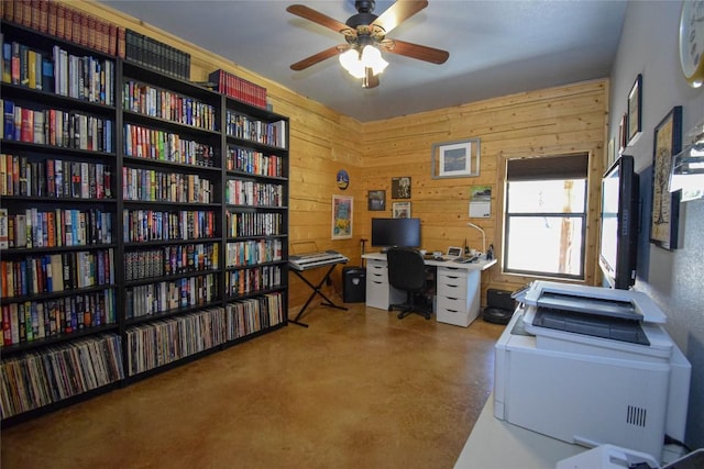 home office with ceiling fan, wood walls, concrete floors, and bookshelves