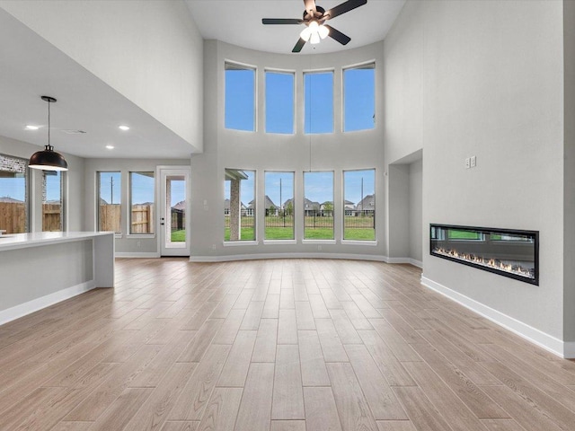 7413 Desert Needle Dr, Lago Vista, TX 78645 - unfurnished living room with light wood finished floors, a ceiling fan, a glass covered fireplace, baseboards, and a towering ceiling