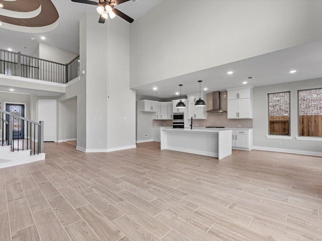 7413 Desert Needle Dr, Lago Vista, TX 78645 - unfurnished living room featuring a towering ceiling, a ceiling fan, light wood-type flooring, baseboards, and a sink