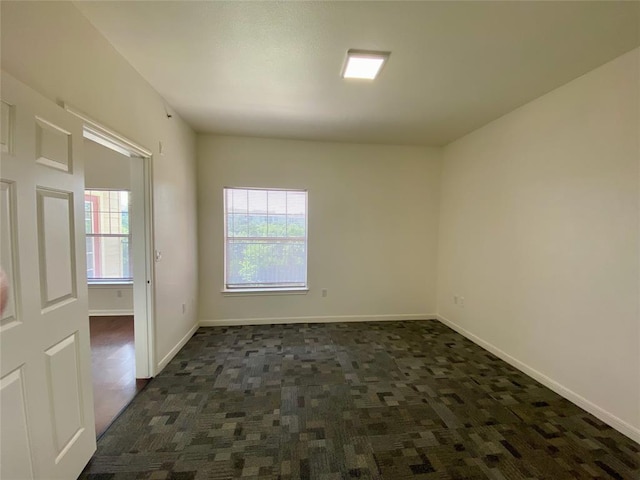 spare room with dark carpet and baseboards