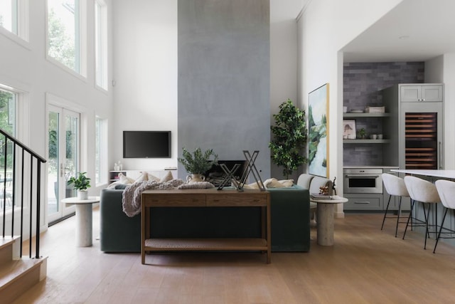 living area with wine cooler, stairs, light wood-style floors, and a towering ceiling