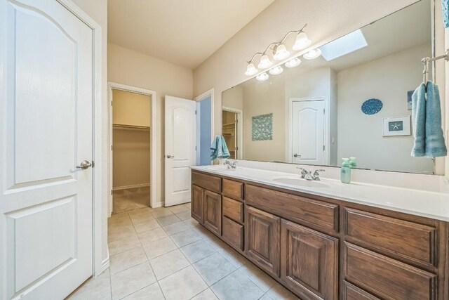 full bath with tile patterned floors, a sink, a skylight, a walk in closet, and double vanity